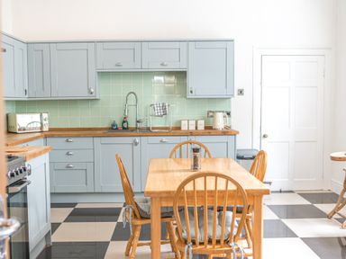 A kitchen with blue cabinets wooden countertops a wooden dining table and chairs with cushions at 8 Corkickle in Whitehaven