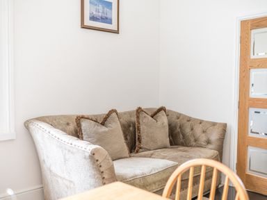 A corner sofa with two cushions below a framed picture and next to a wooden door at 8 Corkickle in Whitehaven