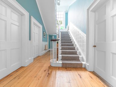 A hallway with wooden floor and white doors leading to a carpeted staircase at 8 Corkickle in Whitehaven