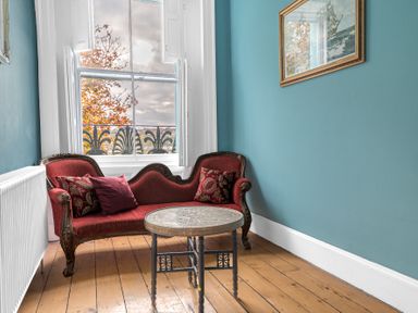 A sitting area with a red upholstered loveseat and a round carved wooden table near a window at 8 Corkickle in Whitehaven