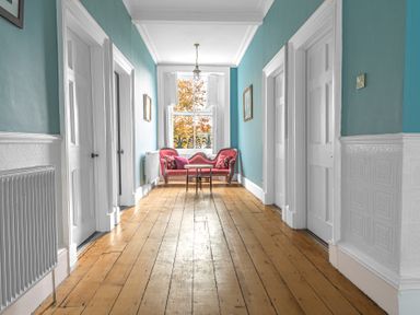 A hallway with blue walls and wooden floor with a red vintage sofa and small table by a window at 8 Corkickle in Whitehaven
