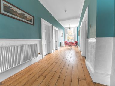 A hallway with wooden floor teal and white walls red sofa and two doors at 8 Corkickle in Whitehaven