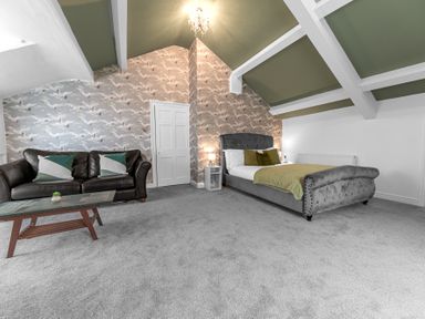 A bedroom with a bed sofa coffee table and patterned wallpaper at 8 Corkickle in Whitehaven