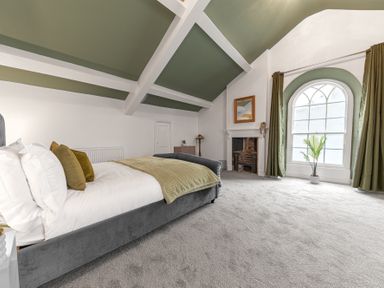 A bedroom with a bed fireplace arched window and green ceiling beams at 8 Corkickle in Whitehaven