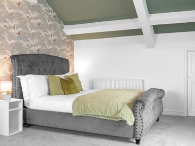 A bedroom with a grey upholstered bed with green pillows and a green throw on the bed at 8 Corkickle in Whitehaven