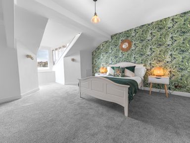 A bedroom with a white bed green cushions tropical wallpaper and two bedside tables at 8 Corkickle in Whitehaven