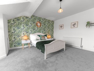A bedroom with a white bed and green blanket against a tropical leaf wallpaper at 8 Corkickle in Whitehaven