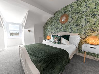 A bedroom with a bed with green bedding and a tiger pillow beside bedside tables with lamps and a large window at 8 Corkickle Whitehaven