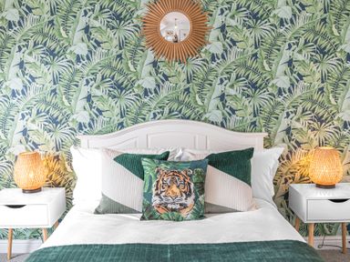 A bedroom with a bed with pillows and a tiger print cushion two bedside tables with lamps and leafy patterned wallpaper at 8 Corkickle in Whitehaven