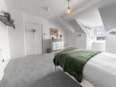 A bedroom with a bed covered with a green blanket a white dresser a wall shelf and a window at 8 Corkickle in Whitehaven
