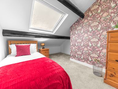 A bedroom with a single bed red blanket and pillow wooden furniture skylight and floral wallpaper at 8 Corkickle in Whitehaven