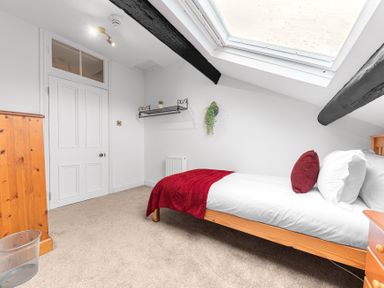 A bedroom with a wooden bed with white bedding and red pillow and blanket a wooden dresser a white door and a skylight window at 8 Corkickle in Whitehaven