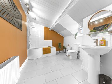 A bathroom with a bathtub shower toilet sink mirror and orange accent wall at 8 Corkickle in Whitehaven