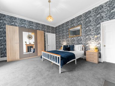 A bedroom with a double bed blue bedding wooden wardrobe and bedside table at 8 Corkickle in Whitehaven