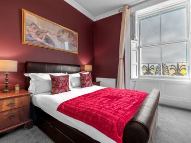 A bedroom with a leather bed frame red bedding bedside tables with lamps and a large window at 8 Corkickle in Whitehaven