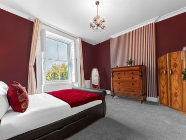 A bedroom with a bed a window with curtains a wooden dresser a mirror and a wooden wardrobe at 8 Corkickle in Whitehaven