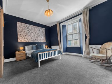 A bedroom with a bed and bedside tables under a window with curtains and a rocking chair at 8 Corkickle in Whitehaven