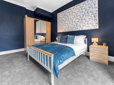 A bedroom with a double bed blue bedding wooden wardrobe and bedside table with lamp at 8 Corkickle in Whitehaven