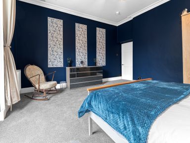 A bedroom with blue walls a bed with blue blanket a rocking chair and a dresser at 8 Corkickle in Whitehaven
