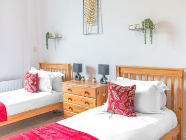 A bedroom with two single wooden beds with white bedding and red pillows at 8 Corkickle in Whitehaven