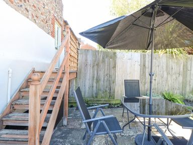 A wooden staircase leading to a door beside a patio area with black chairs and a glass table with a black umbrella at Crab Corner in Wells-Next-The-Sea