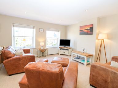 A living room with brown leather sofas a television on a stand and a floor lamp at Crab Corner in Wells-Next-The-Sea