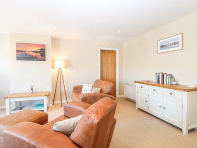 A living room with leather armchairs a wooden coffee table a floor lamp and a white sideboard with books at Crab Corner in Wells-Next-The-Sea