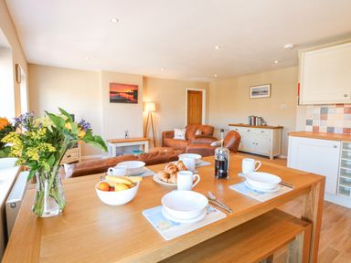 A dining table set with bowls cups croissants and fruit in an open plan kitchen and living room at Crab Corner in Wells-Next-The-Sea