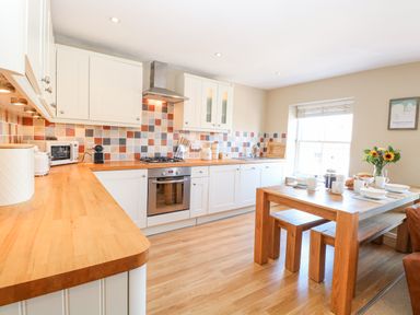 A kitchen with wooden countertops white cabinets a wooden dining table with bench seating and a vase of flowers at Crab Corner in Wells-Next-The-Sea
