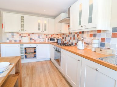 A kitchen with white cabinets wooden countertops and multicolored tiled backsplash at Crab Corner in Wells-Next-The-Sea