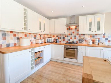 A kitchen with white cabinets wooden countertops a tiled backsplash and various small appliances at Crab Corner in Wells-Next-The-Sea