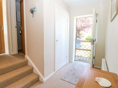 A hallway with beige carpeted stairs leading to doors and a glass door opening to a garden at Crab Corner in Wells-Next-The-Sea
