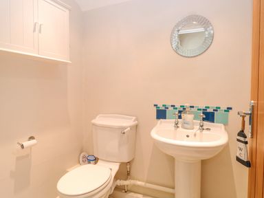 A bathroom with a toilet a pedestal sink with soap a round mirror and wall-mounted cabinet at Crab Corner in Wells-Next-The-Sea