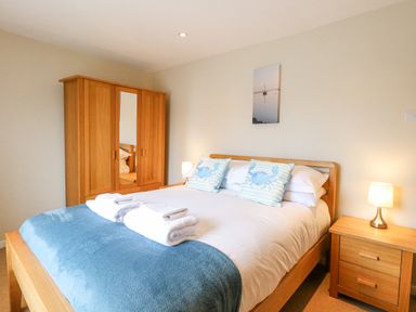 A bedroom with a wooden bed and wardrobe two blue crab patterned cushions on the bed and bedside table lamps at Crab Corner in Wells-Next-The-Sea