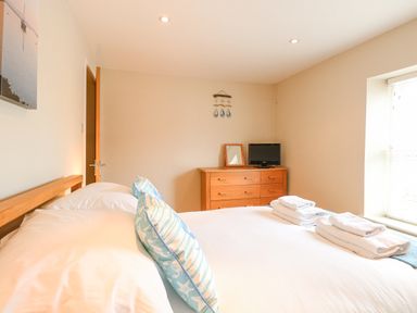 A bedroom with a bed with pillows and towels a dresser with a mirror and television and a window with blinds at Crab Corner in Wells-Next-The-Sea