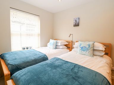 A bedroom with two single beds with blue throws and crab design cushions at Crab Corner in Wells-Next-The-Sea