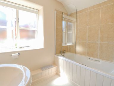 A bathroom with a bathtub shower combination a window and a sink at Crab Corner in Wells-Next-The-Sea