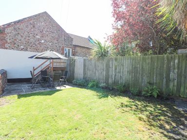 A garden with outdoor table and chairs under an umbrella near a wooden fence at Crab Corner in Wells-Next-The-Sea
