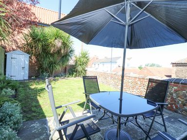 A garden with a patio table umbrella and chairs near a lawn and a small shed at Crab Corner in Wells-Next-The-Sea