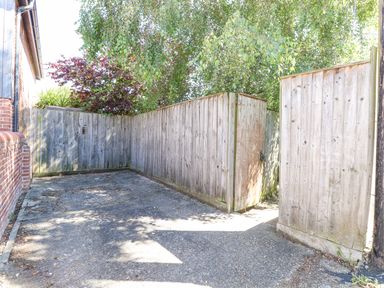 An outdoor area with a concrete ground and wooden fences surrounded by trees at Crab Corner in Wells-Next-The-Sea