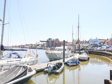 A harbor with several boats docked along the piers and buildings in the background at Crab Corner in Wells-Next-The-Sea