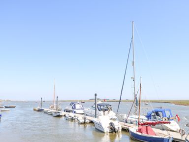A marina with several boats docked along a wooden pier on a calm river at Crab Corner in Wells-Next-The-Sea
