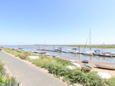 A river with boats moored along the shore next to a paved path at Crab Corner in Wells-Next-The-Sea
