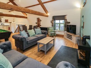 A living room with blue sofas a coffee table a plaid armchair a television on a cabinet a pool table and wooden beams at The Barn by Lyons in Talybont near Barmouth