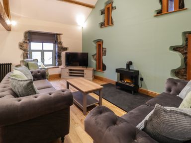 A living room with two sofas a coffee table a TV and a stove at The Barn by Lyons Talybont near Barmouth