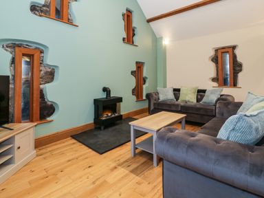 A living room with a wooden floor sofas cushions a small fireplace and irregular windows at The Barn by Lyons Talybont near Barmouth