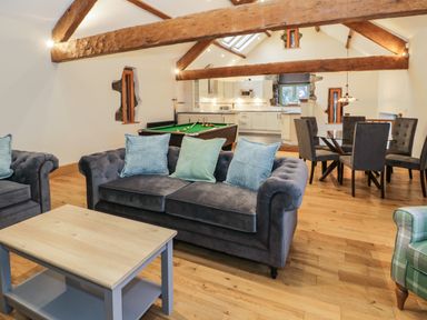 An open living room with sofas, a coffee table, a pool table, a dining table with chairs, and a kitchen area at The Barn by Lyons Talybont near Barmouth