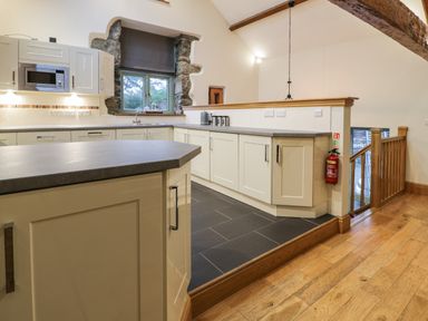 A kitchen with white cabinets gray countertops a window with stone framing and wooden floors at The Barn by Lyons in Talybont near Barmouth