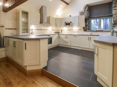 A kitchen with cream cabinets a gray countertop a stove oven microwave and a window with stone surrounds at The Barn by Lyons in Talybont near Barmouth