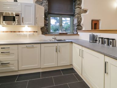 A kitchen with white cabinets stainless steel microwave sink and kettle on countertop at The Barn by Lyons in Talybont near Barmouth